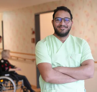 Pflegehelfer bei PFLEGEN & WOHNEN HAMBURG unterstützt Bewohnerin im Rollstuhl in Pflege, Betreuung und Wohlbefinden.