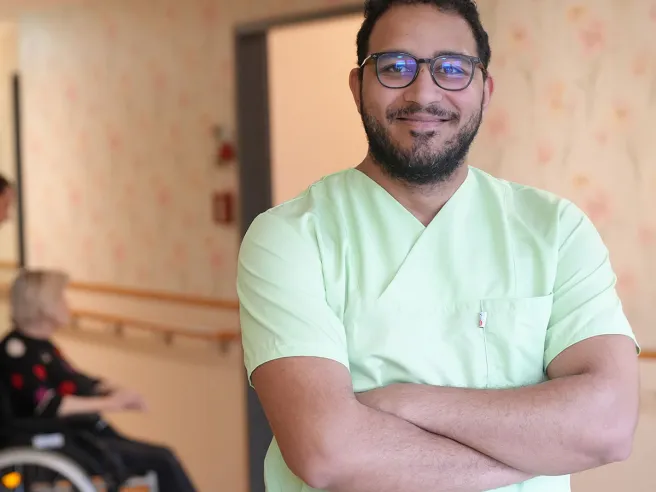 Pflegehelfer bei PFLEGEN & WOHNEN HAMBURG unterstützt Bewohnerin im Rollstuhl in Pflege, Betreuung und Wohlbefinden.